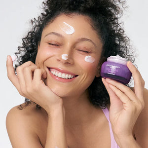 Woman applying cream to her face with a purple jar of Skinceuticals product.